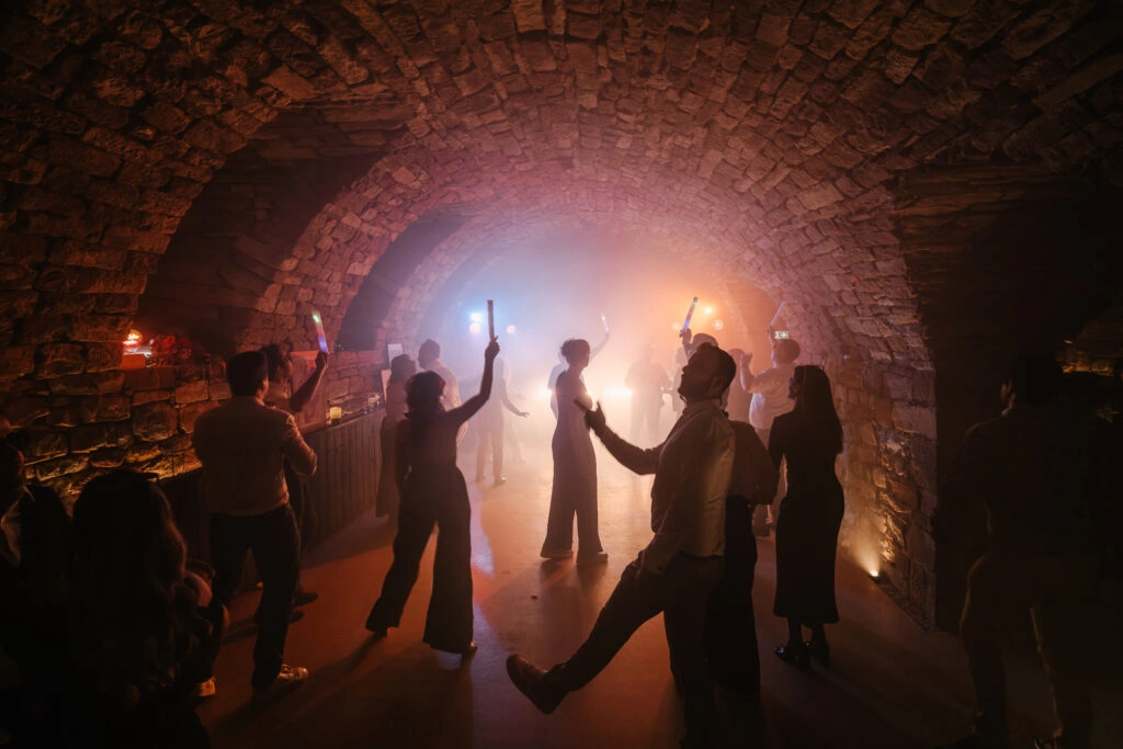 Des invités dansent les bras levés sous une voûte éclairée de lumières chaudes.
