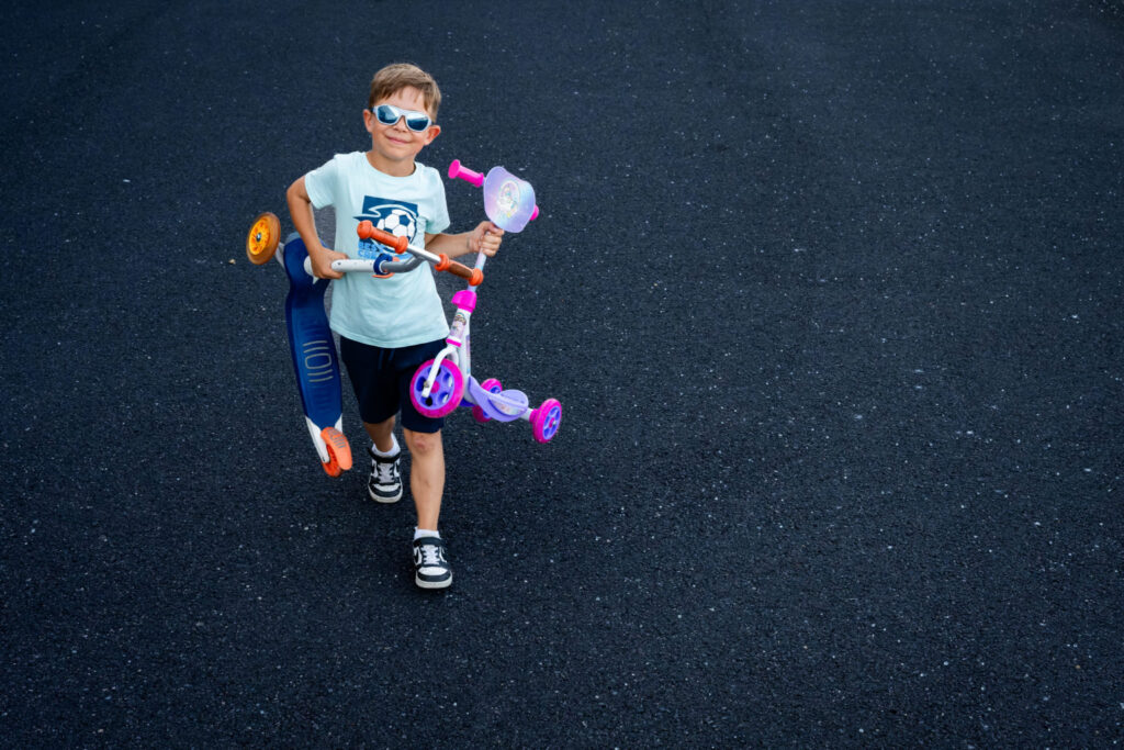 Un garçon en lunettes de soleil porte une trottinette violette sur l’épaule