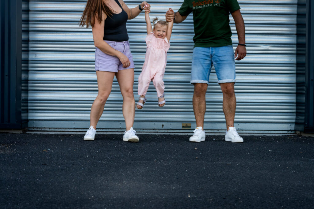 Des parents soulèvent leur petite fille par les mains devant une porte métallique