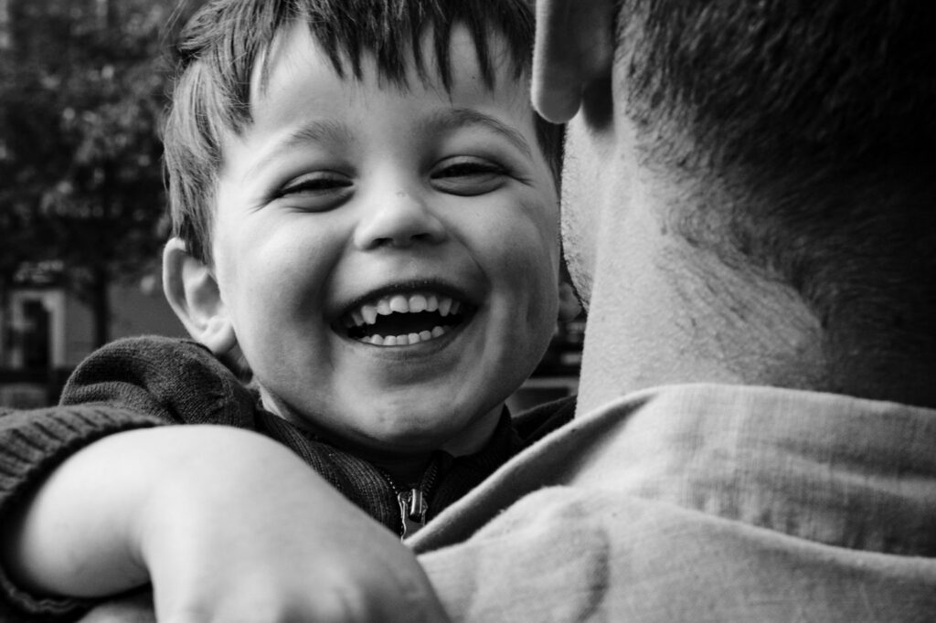 Un petit garçon rit dans les bras d’un adulte, en noir et blanc