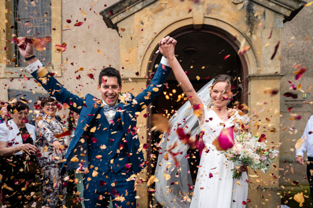 Les mariés sortent sous une pluie de confettis, les mains levées