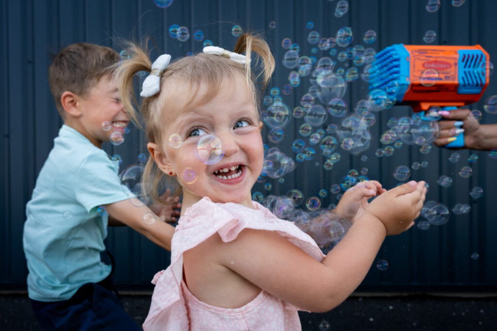 Une petite fille sourit au milieu des bulles, avec un garçon derrière elle