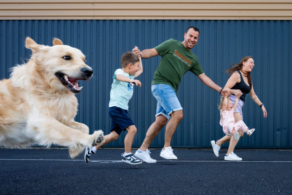 Une famille court devant un mur bleu avec son chien au premier plan