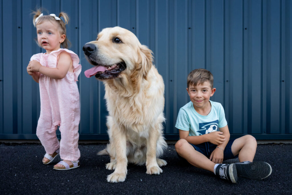Deux enfants posent avec un grand chien devant un mur bleu