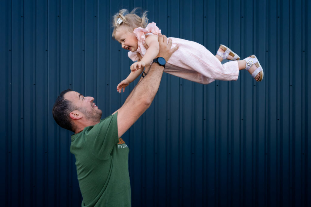 Un père soulève sa petite fille devant une façade bleue