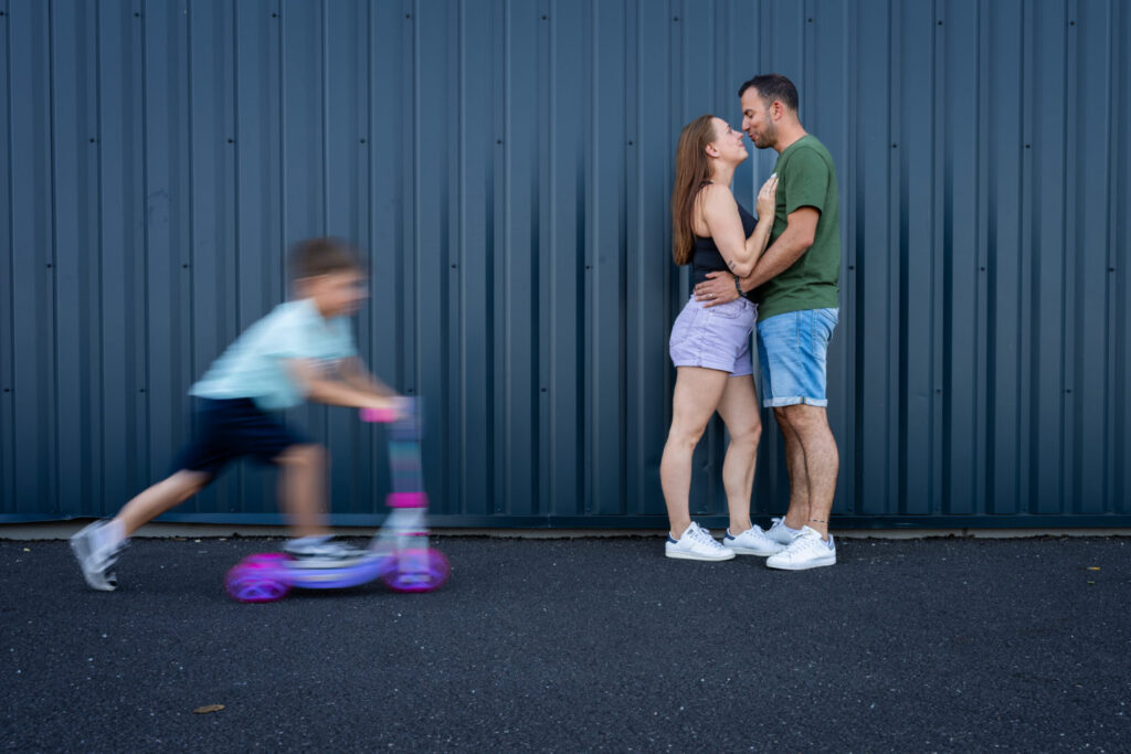 Un enfant passe en trottinette devant ses parents qui s’embrassent