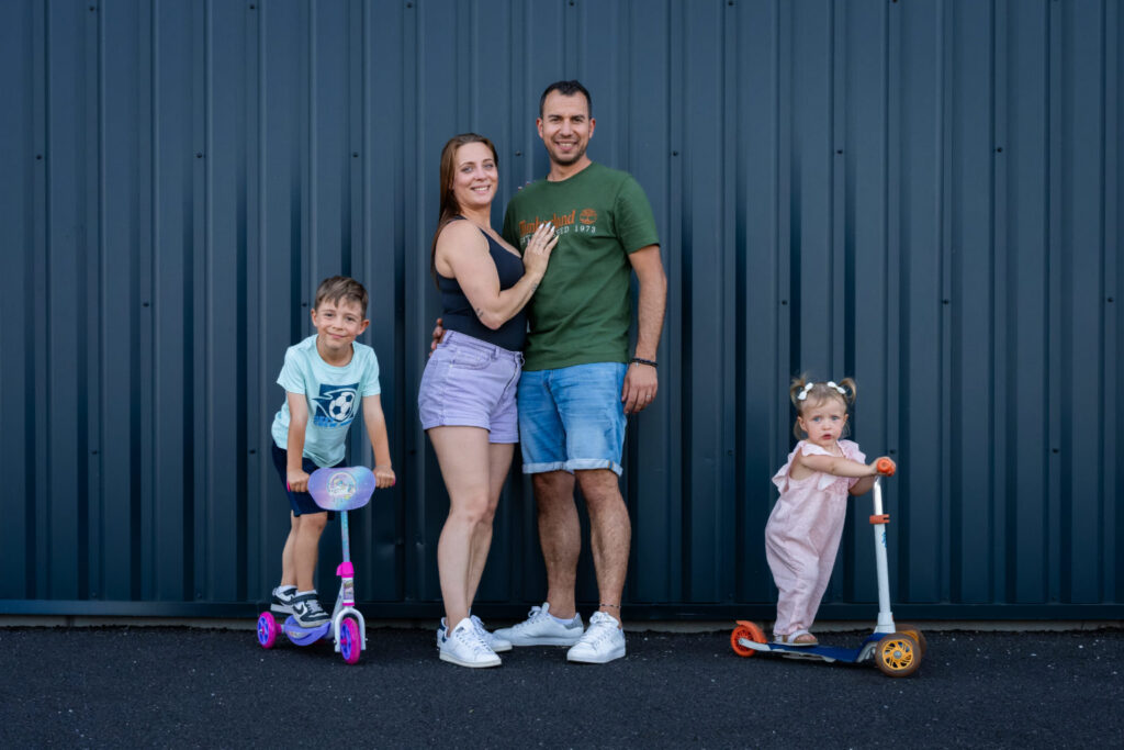 Une famille pose avec deux trottinettes devant une façade bleue