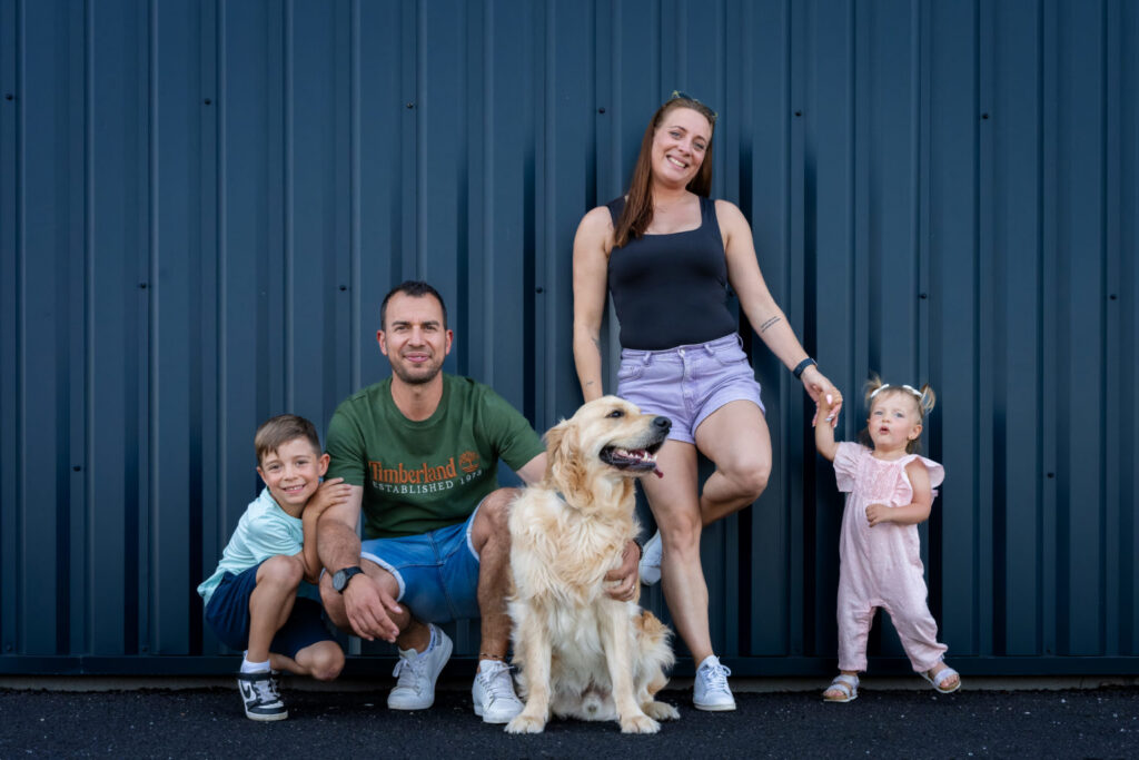 Une famille pose avec son chien devant un mur bleu