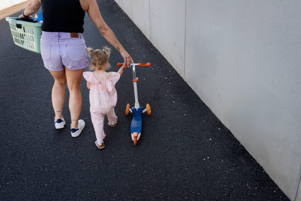 Une petite fille marche en tenant la main d’un adulte, sa trottinette à côté