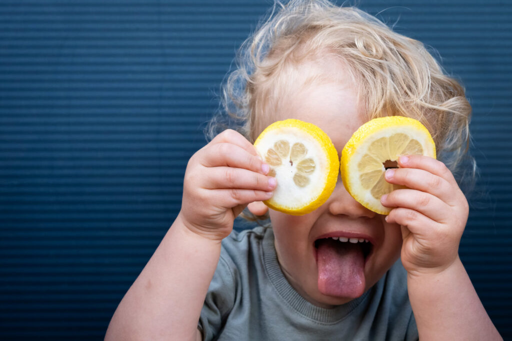 Une petite fille tire la langue avec des rondelles de citron devant les yeux