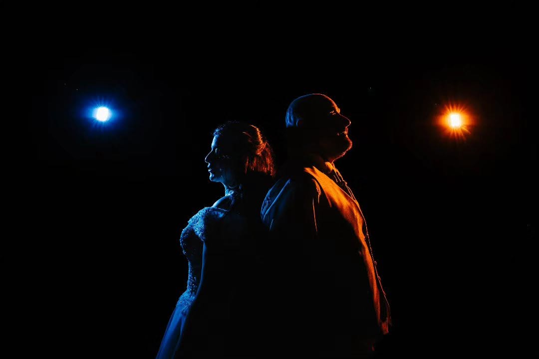 Les silhouettes de Priscillia et Patrice se détachent dans la nuit entre des lumières bleue et orange.