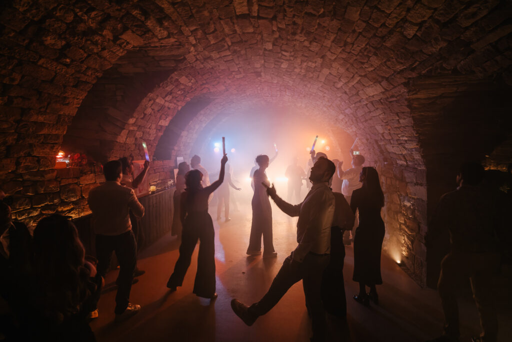 Des invités dansent les bras levés sous une voûte éclairée de lumières chaudes.