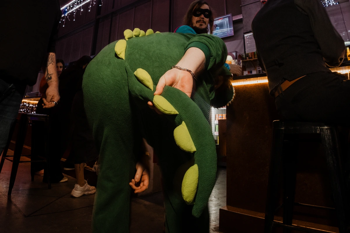 Jonathan de dos dans son déguisement de dinosaure vert, tenant la queue du costume